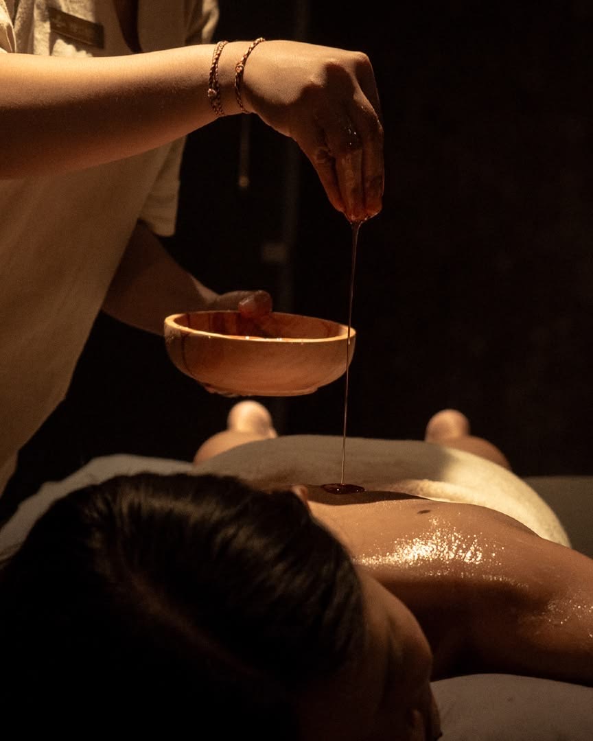 Manos de la terapeuta vertiendo aceite tibio sobre la espalda durante un masaje